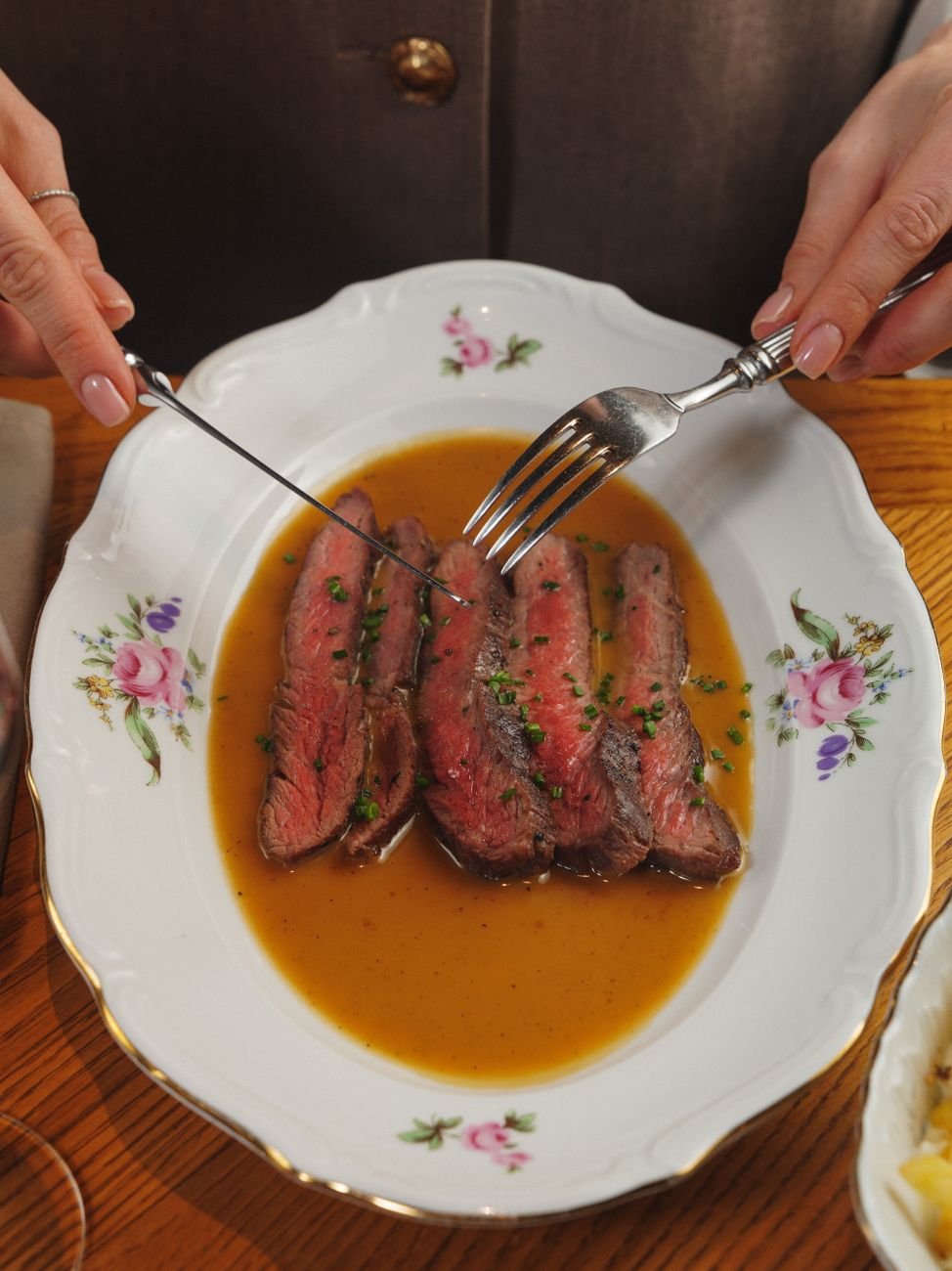Sliced steak served in sauce on a floral plate, ready for dining.