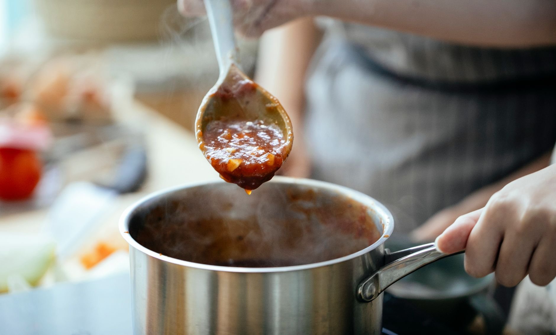 Cooks in aprons preparing sauce in a saucepan in a kitchen
